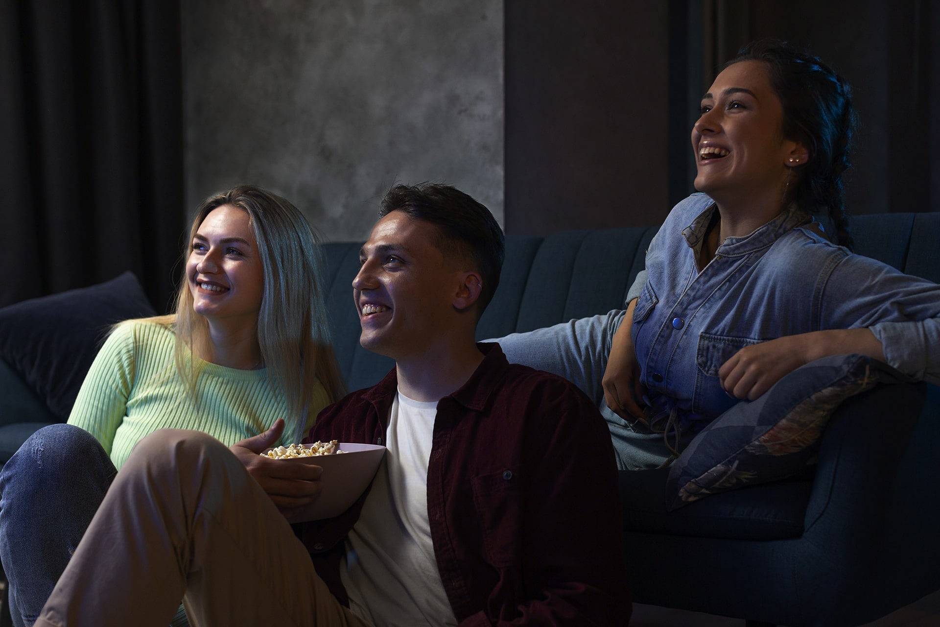 Three friends laughing together on a sofa while watching a film at home